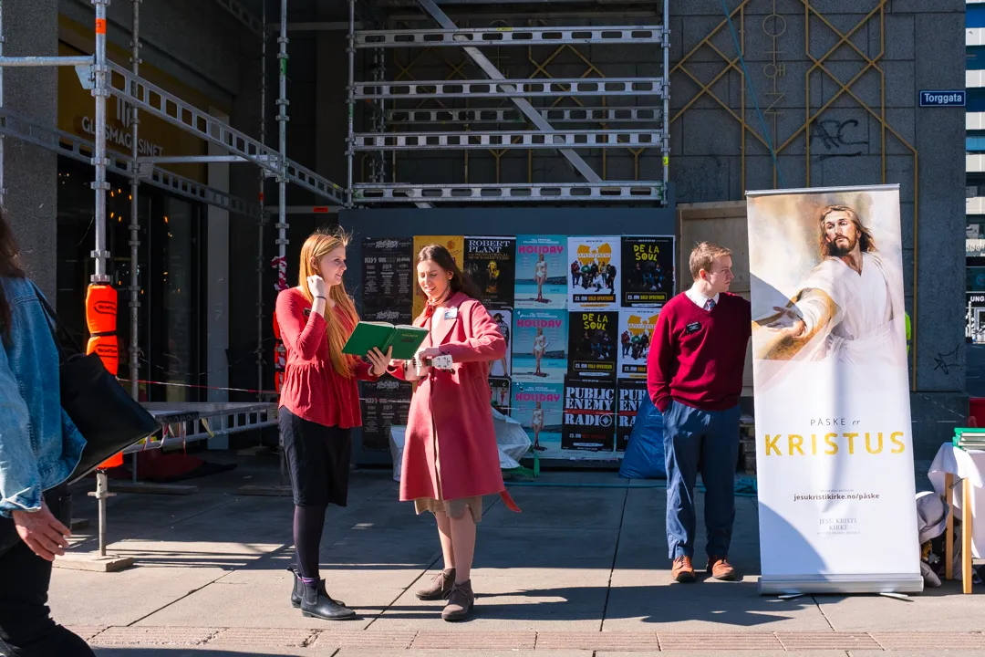 Three young people gathered by a religious street stand