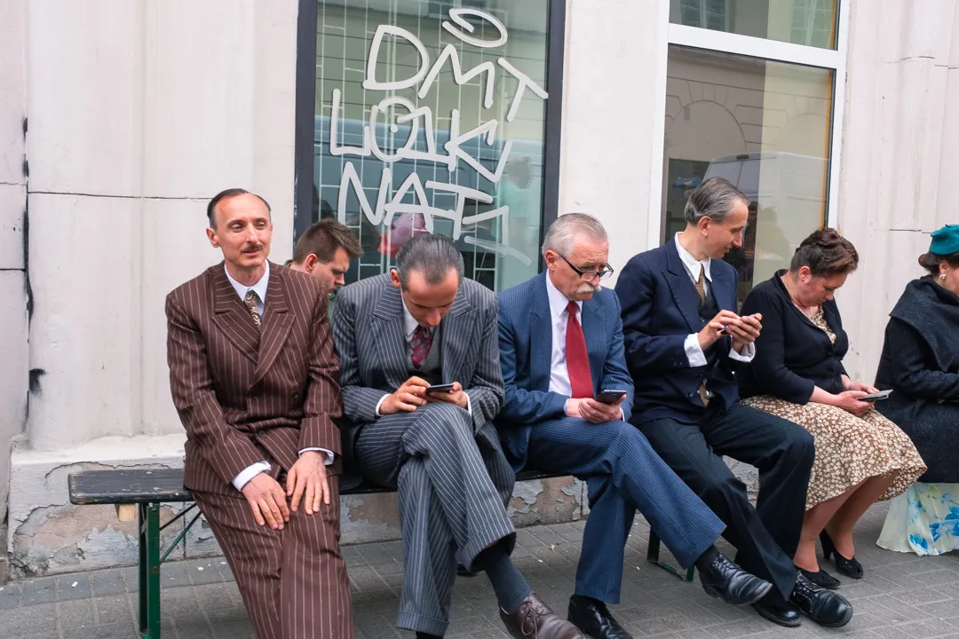Five people seated on a bench, one looking away from a phone